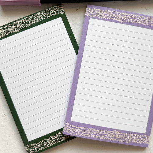 Two notepads with decorative borders and three pens on a white surface