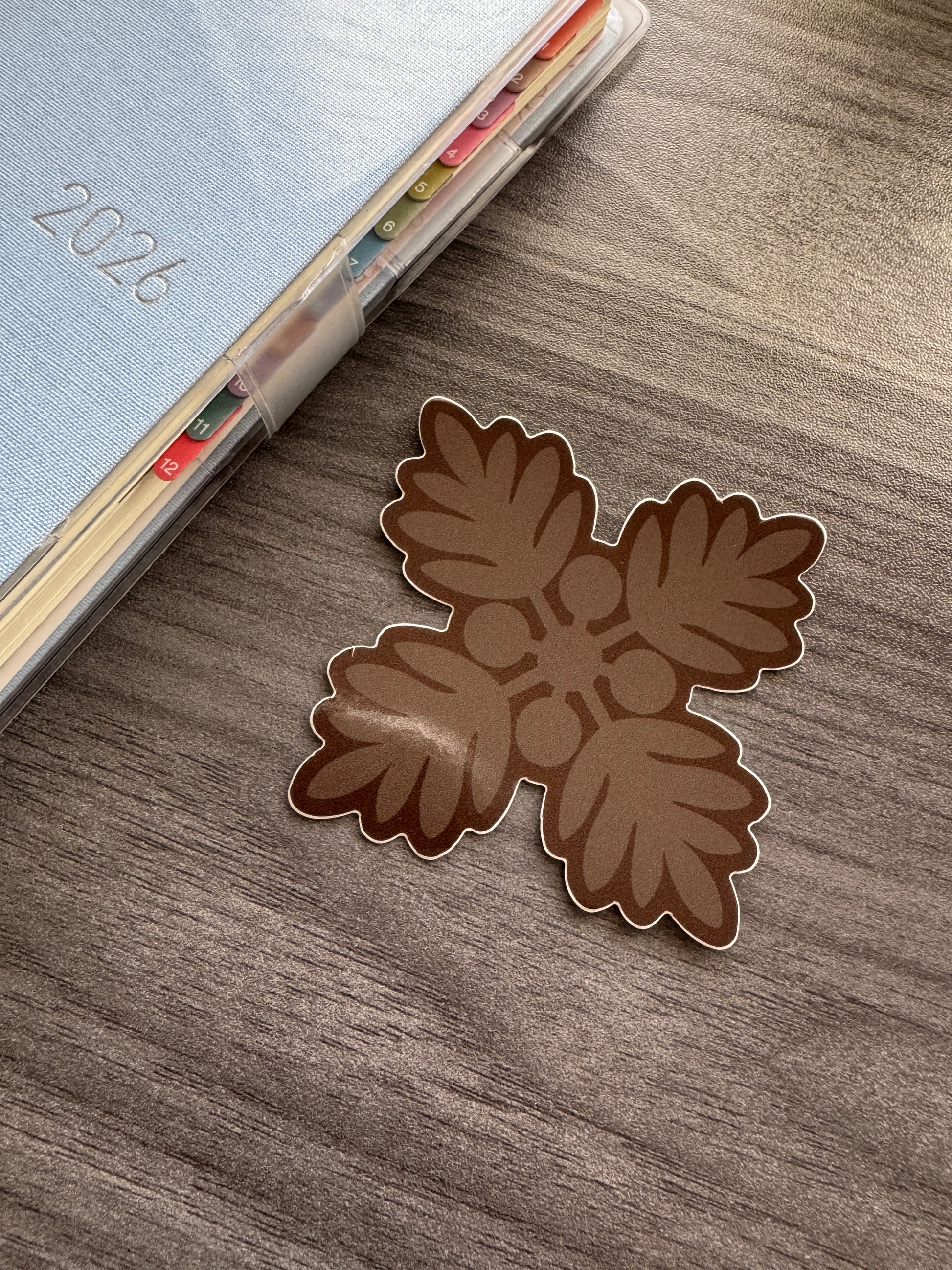 A brown ulu quilt decorative sticker shown on a gray wood-grain surface next to a 2026 planner.
